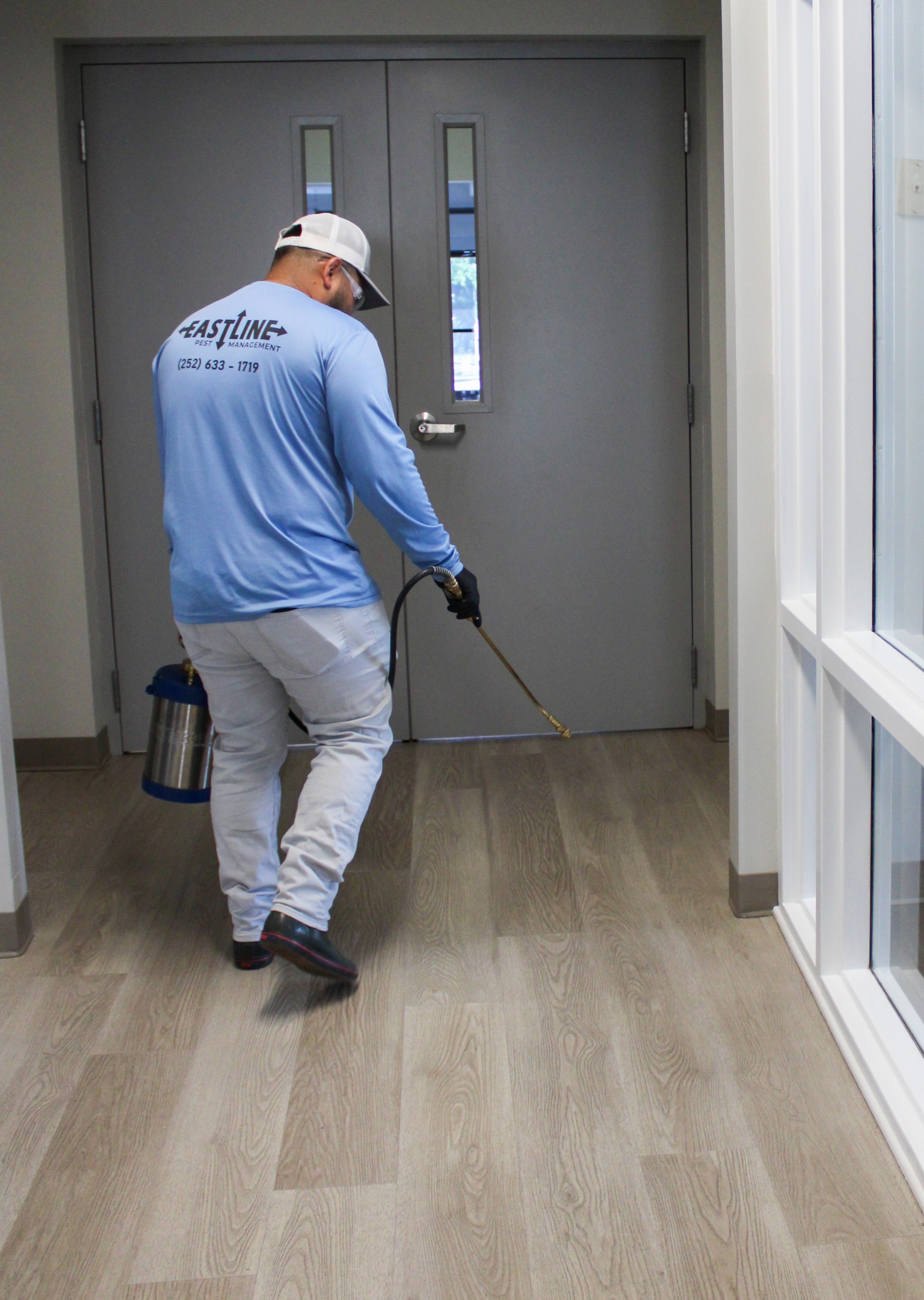 Eastline technician treating commercial hallway and doorway entry points for pest control in New Bern NC