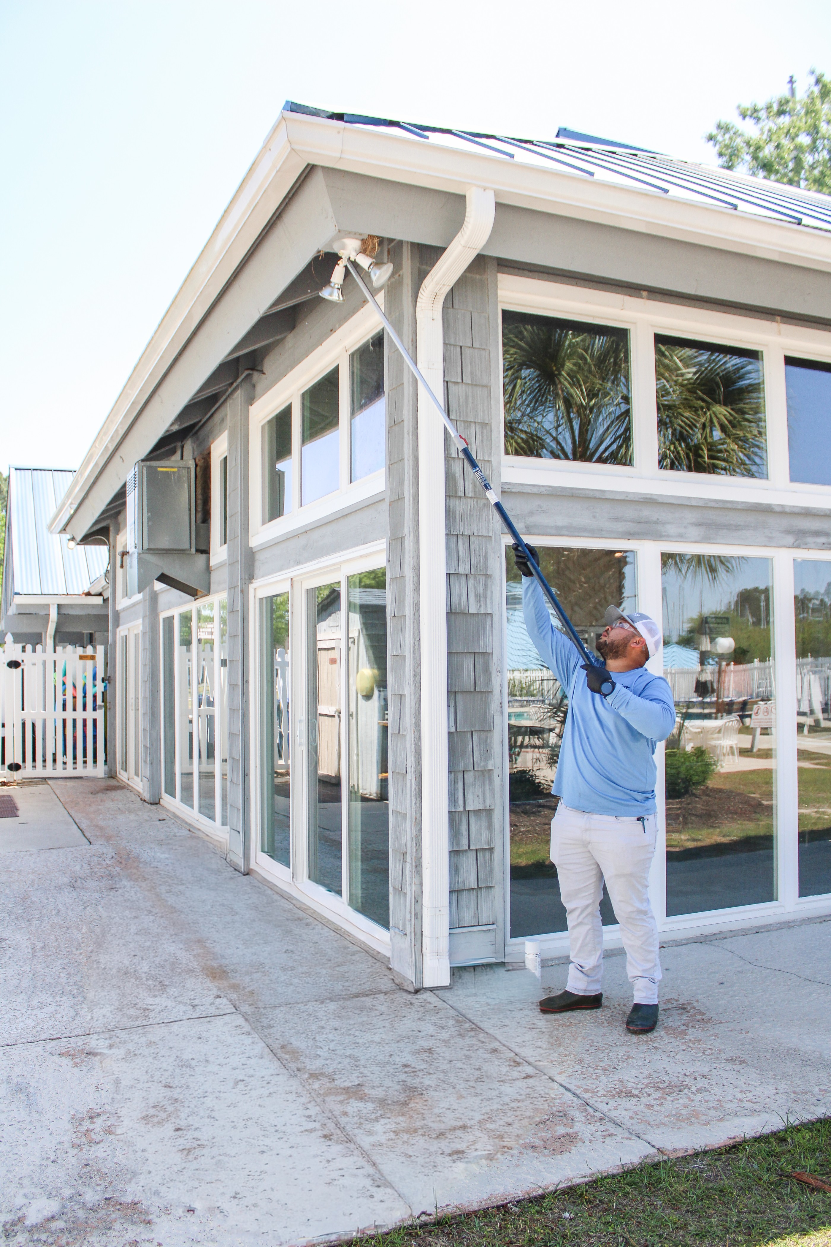 Eastline Pest Management technician reaching high gable peaks with an extension pole to remove spider webs from a residential property in New Bern NC