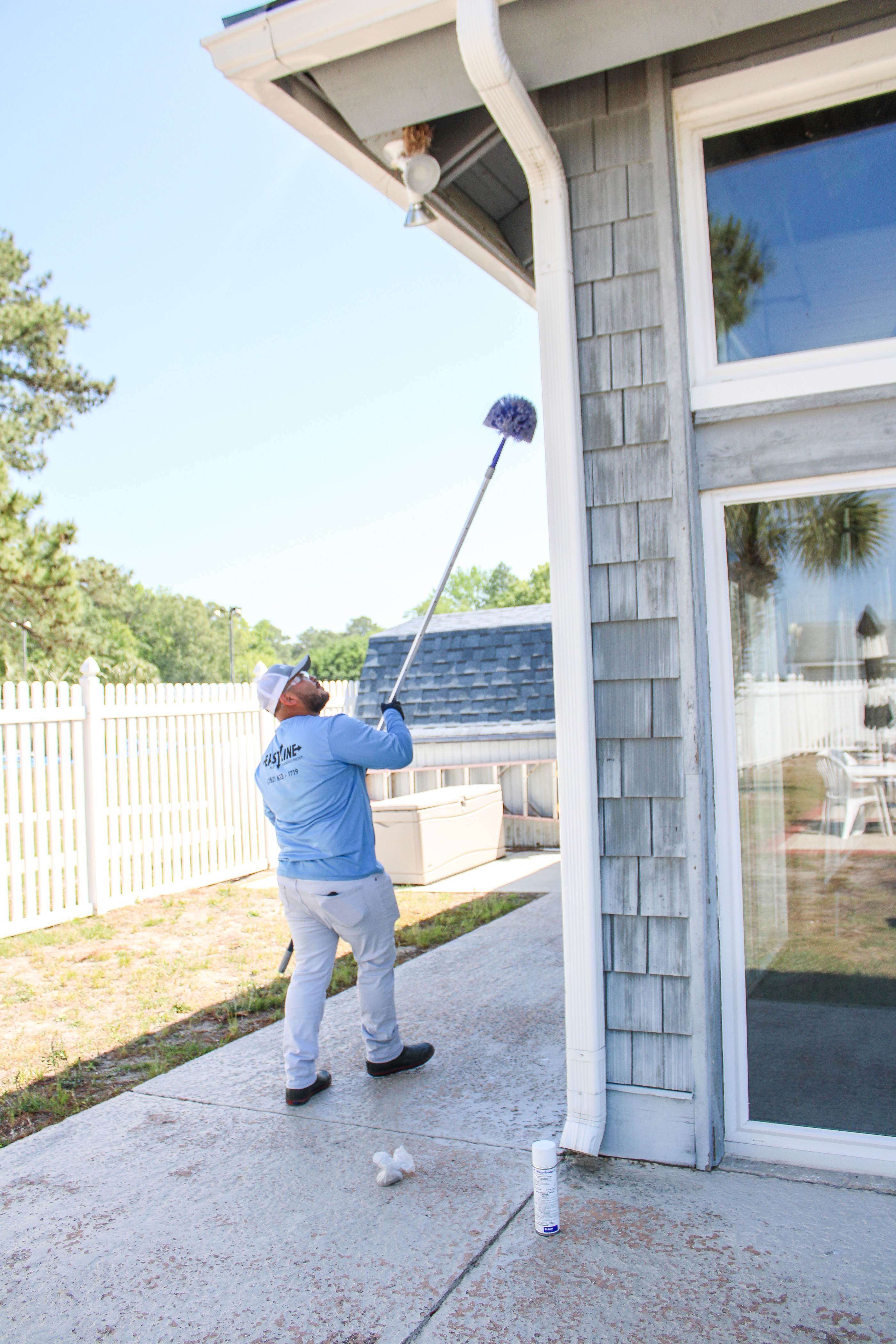Eastline Pest Management technician using an extension pole to deweb spider webs from the eaves and soffits of a New Bern NC home